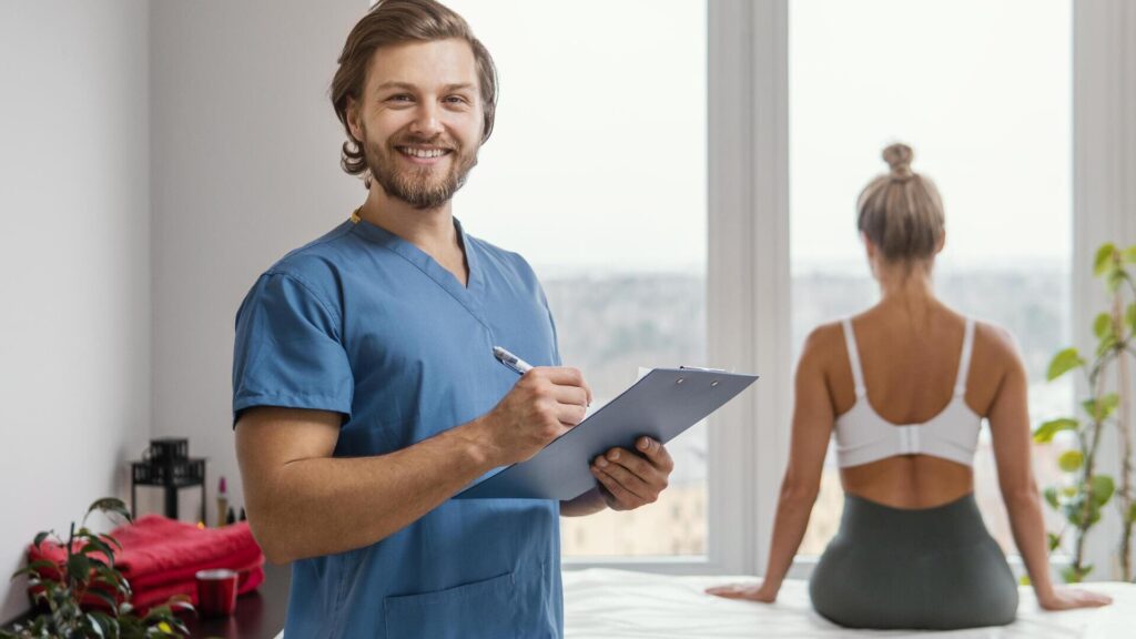 Lächelnder Physiotherapeut mit einer Patientin, die mit dem Rücken zum Betrachter im Hintergrund sitzt